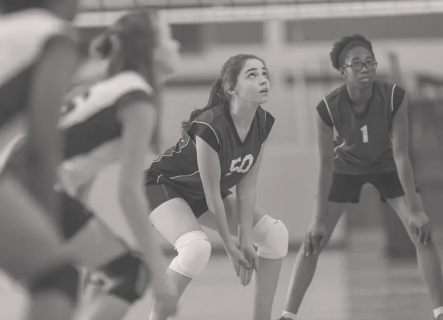 high school female students playing volleyball preparing to receive a serve